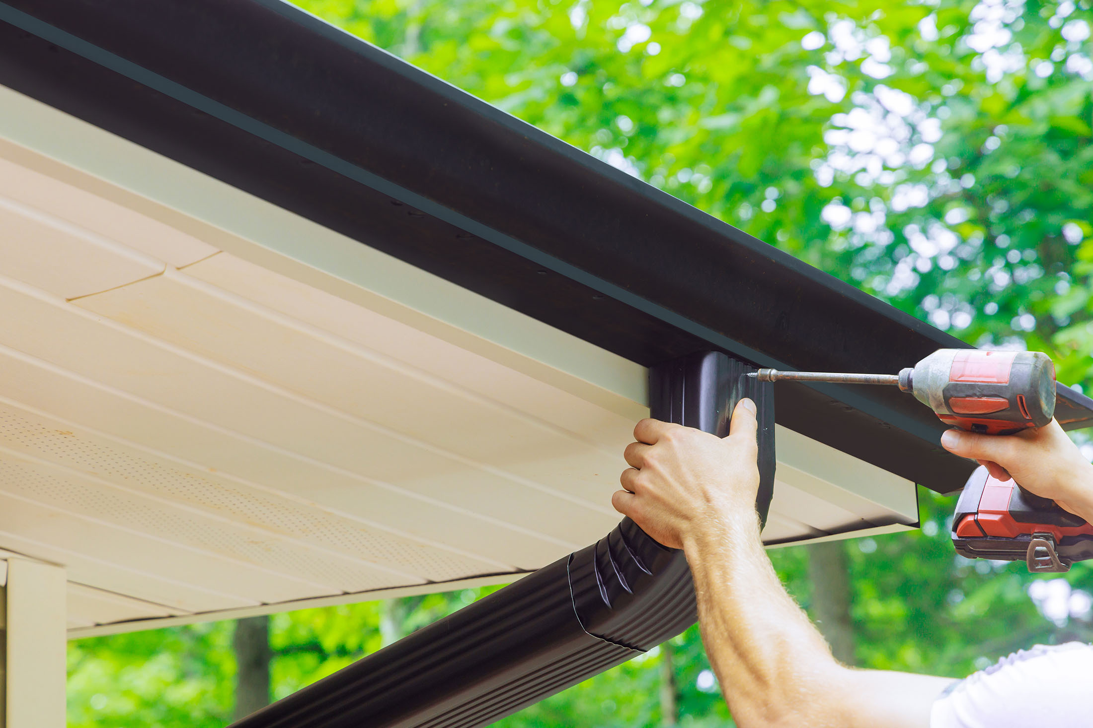 Worker with drill installing gutters and downspout